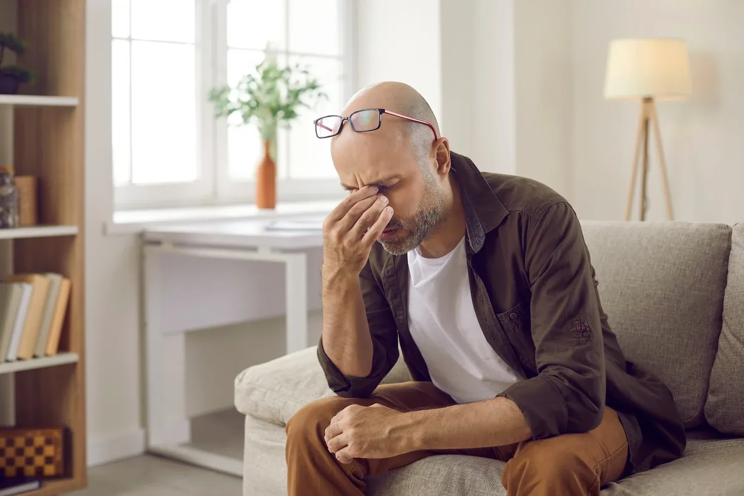 Middle-aged man sitting on a couch with his hand on his face, appearing stressed or overwhelmed.