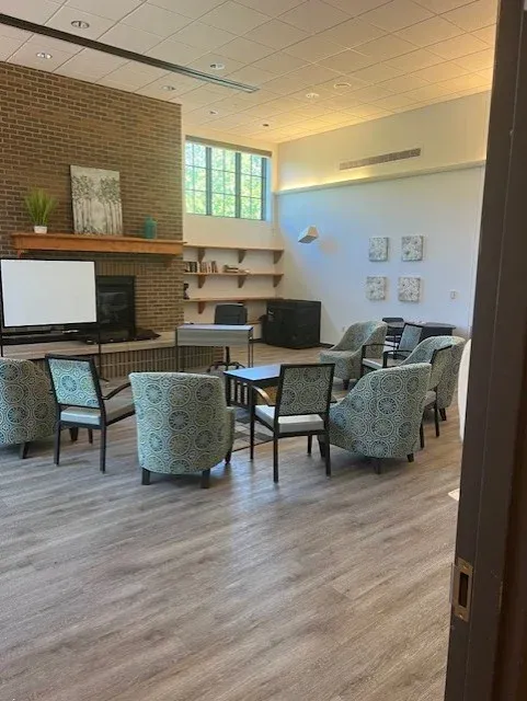 A lounge at Cedar Grove Recovery with upholstered chairs around small tables beside a brick fireplace wall