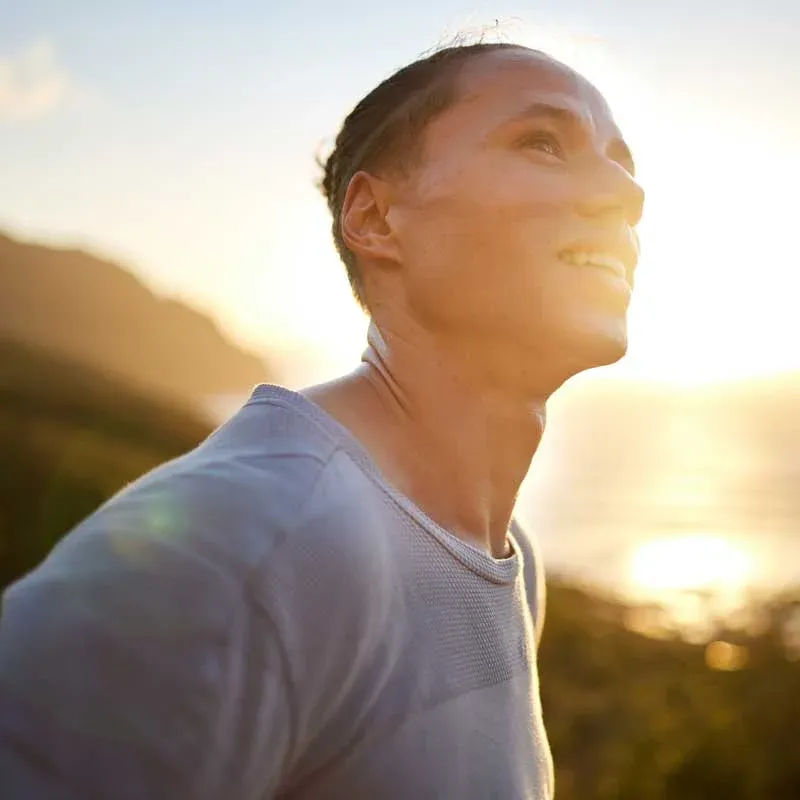 a hiker looks up at the sunset at the top og a mountain or hill