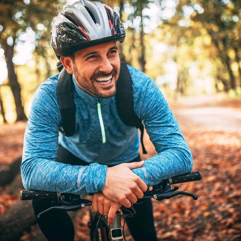 a man pauses his bike ride through the park to smile at the camera