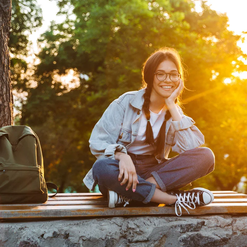 a woman with a backpack sits on a railing at a park