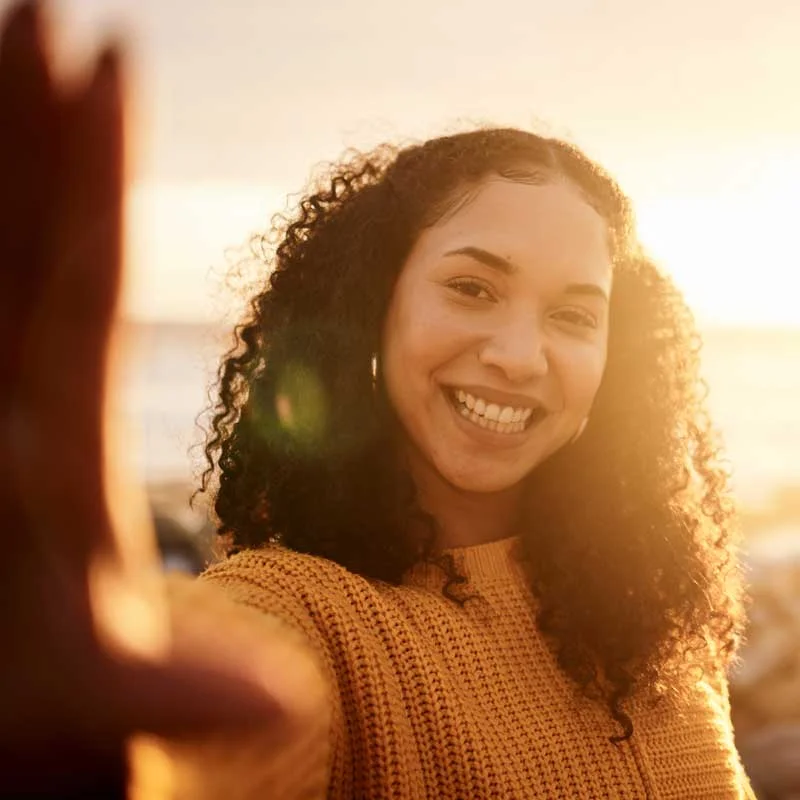 a woman in a yellow sweater smiles at the camera at sunset