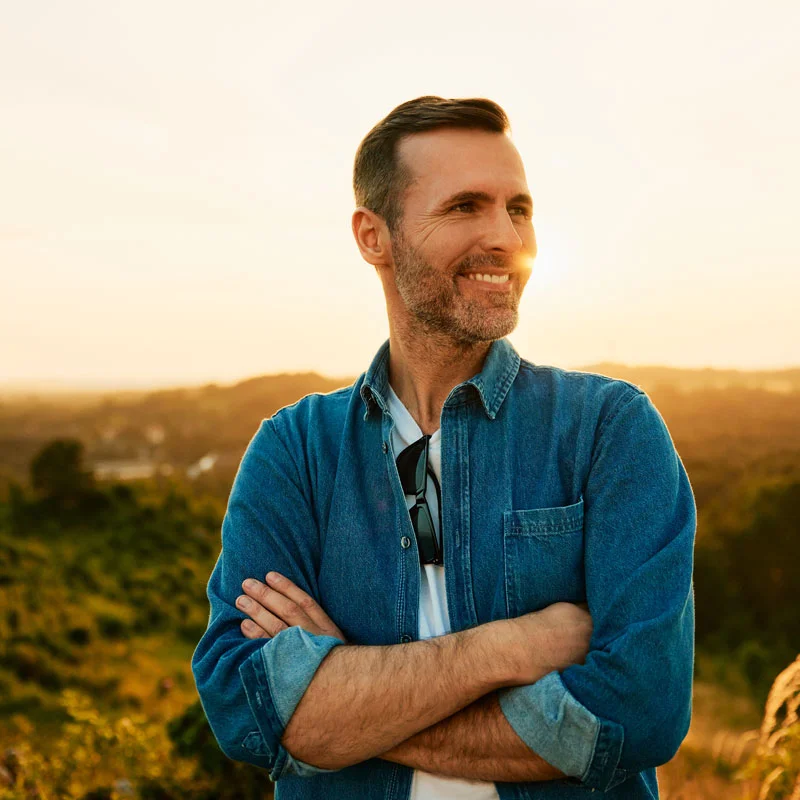a man on top of a hill smiles as he looks at something out of frame