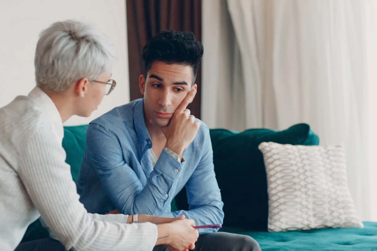 A man listens thoughtfully during a counseling session as a therapist speaks to him in a calm, private setting.