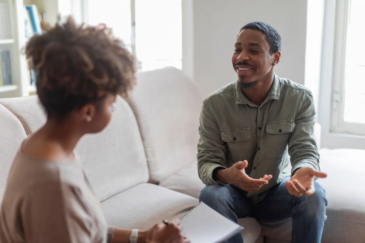 A man smiles while talking with a therapist who takes notes during an open and positive counseling session.