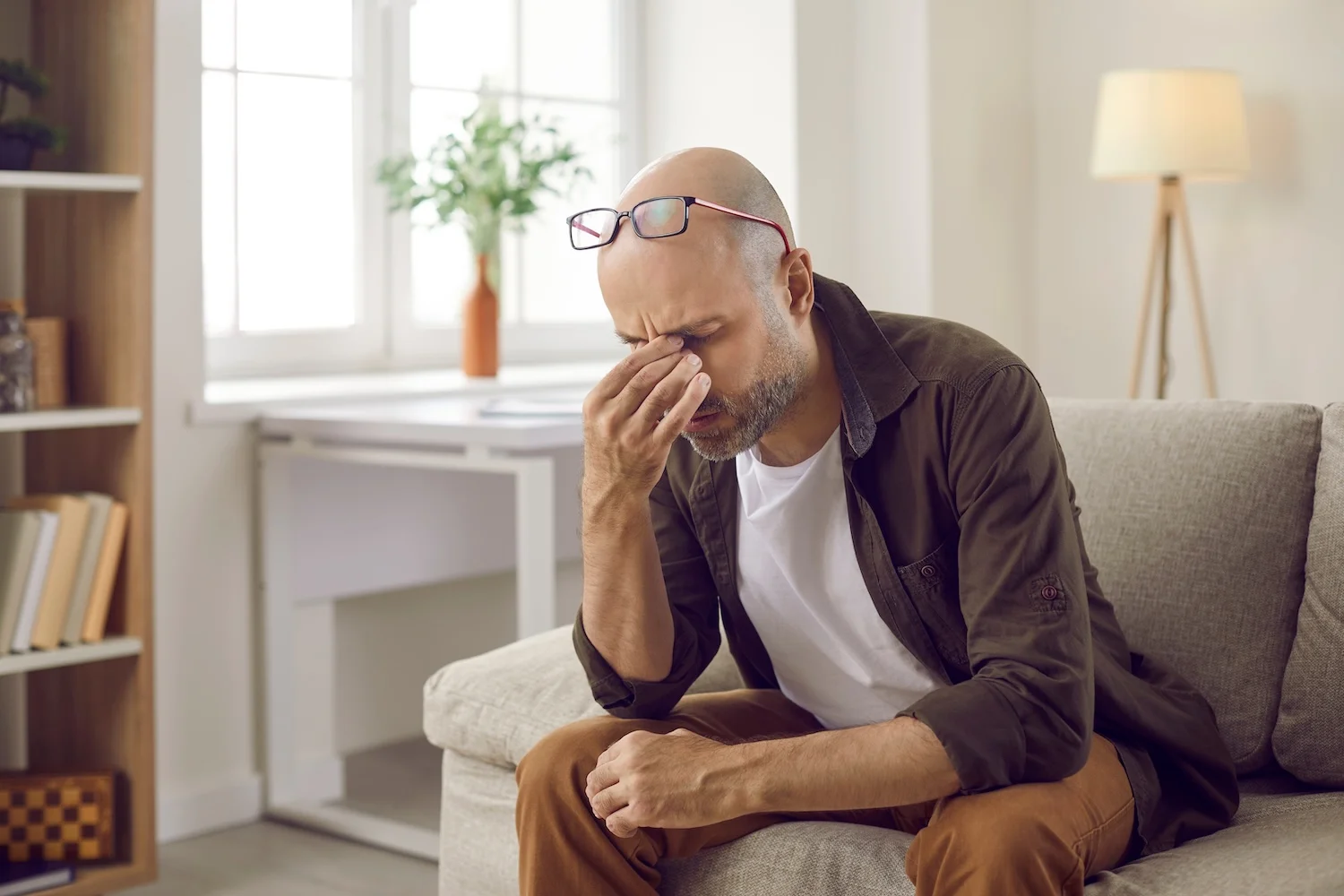 Middle-aged man sitting on a couch with his hand on his face, appearing stressed or overwhelmed.