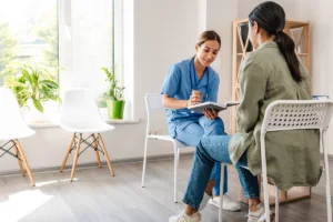 Doctor in blue scrubs sitting across from patient at table prescribing treatment medication